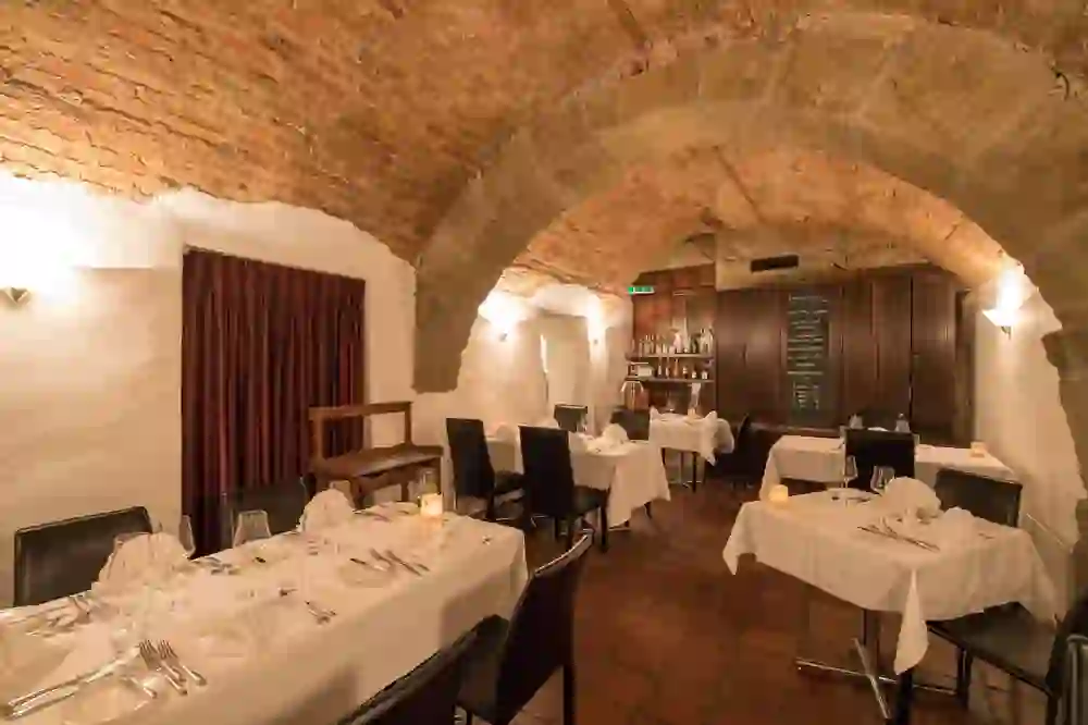 The photo shows the restaurant Wein und Sein in Bern with its rustic charm, which is housed in a vaulted room. The red bricks of the ceiling, the warm wall lights and the carefully laid tables with white tablecloths create a cosy and warm atmosphere. The ambience combines historical architecture with modern comfort, promising an inviting place for an intimate dinner.