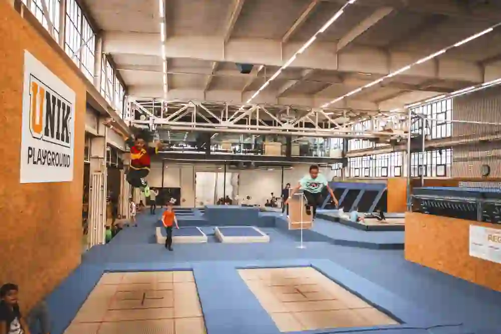 The picture shows a lively trampoline park with children jumping in the air and radiating joy. The large, bright hall with various trampolines and obstacles creates a dynamic and energetic atmosphere that invites children to play and try things out.