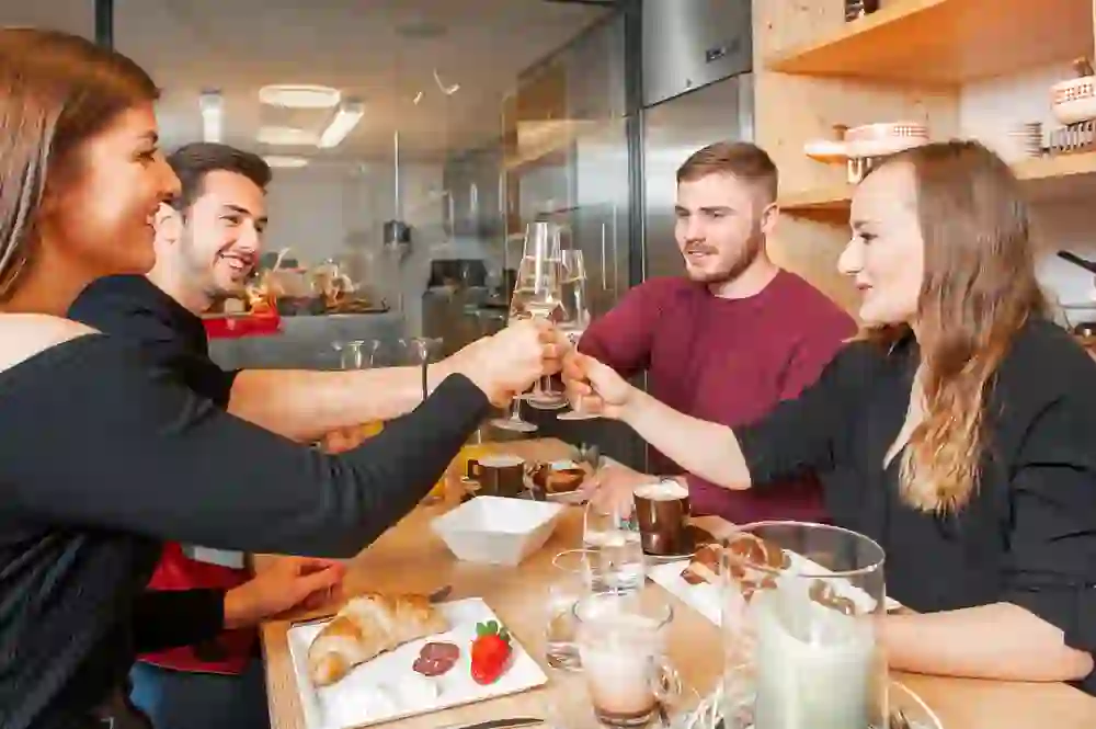 L'image capture un moment joyeux où des amis trinquent en toute convivialité lors d'un brunch, accompagné d'une abondance de délices, ce qui dégage de la chaleur et un sentiment de communauté.