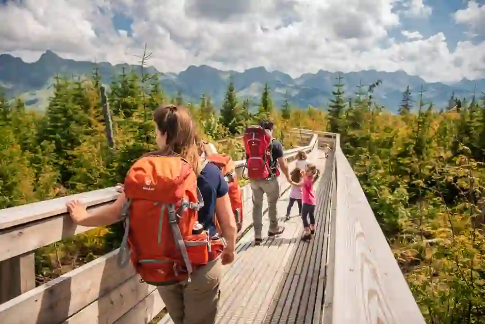 Das Bild zeigt eine Familie auf einer Wanderung über den Gäggersteg im Naturpark Gantrisch. Die warme Sonne, die blühende Vegetation und die mächtigen Berge im Hintergrund verleihen dem Augenblick ein Gefühl von Verbundenheit mit der Natur.