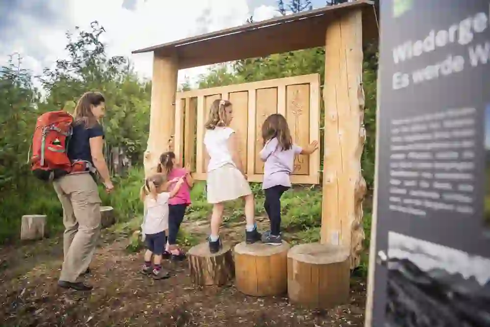 Das Foto zeigt eine Gruppe von Kindern und eine erwachsene Begleitperson, die eine interaktive Station im Gäggersteg Naturpark Gantrisch erkunden.