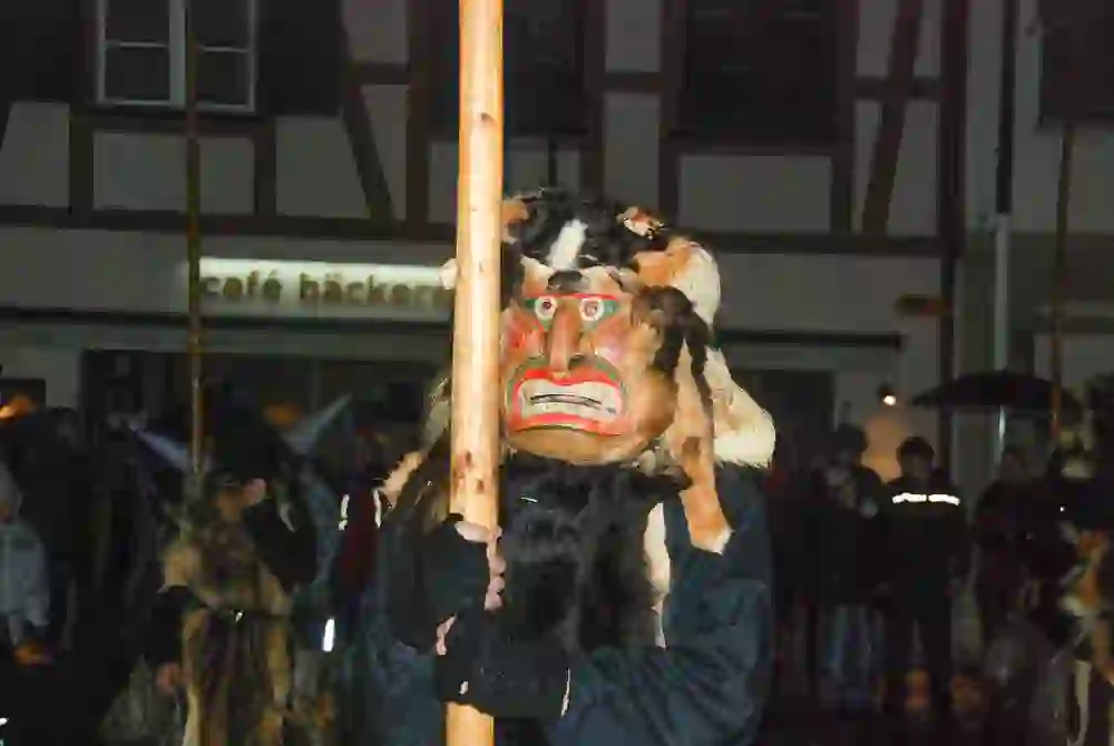 A person in a traditional mask in a parade at night, surrounded by spectators, creates a mysterious and culturally rich atmosphere.