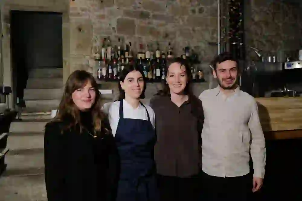 La foto ritrae il team del ristorante Cima di Berna, in posa davanti all'elegante bar con parete in pietra naturale e portabottiglie. L'atmosfera è calda e orgogliosa: un momento pieno di comunità, creatività e passione culinaria.