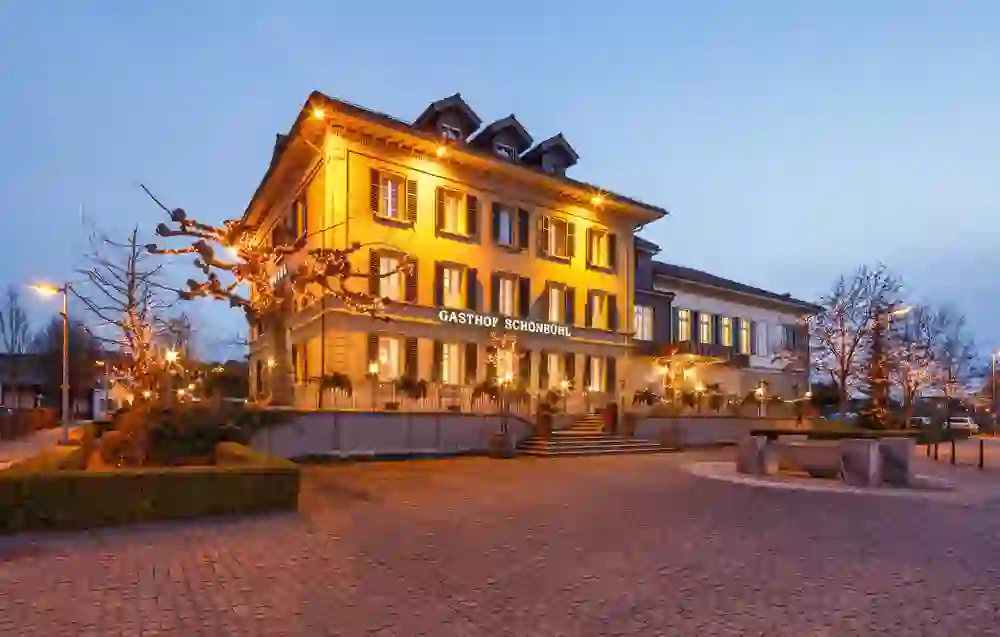 An atmospherically lit country inn that radiates warmth and hospitality at dusk. The elegant façade and festively decorated trees create an inviting atmosphere for guests.