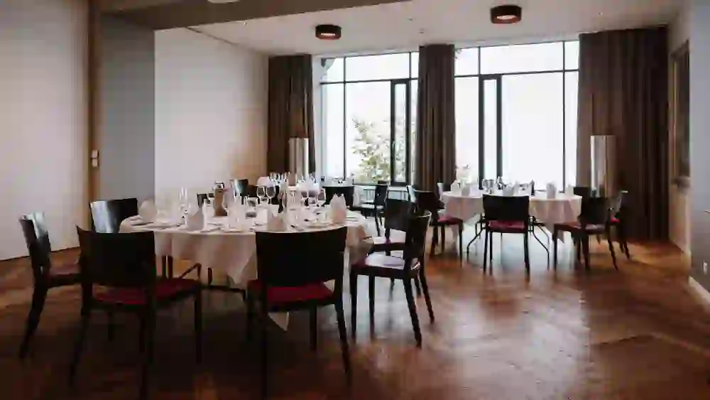Des tables finement dressées sont visibles dans une élégante salle du Gurten Park. De grandes fenêtres laissent entrer la lumière du jour et offrent une vue sur la nature, ce qui crée une atmosphère de calme haut de gamme.