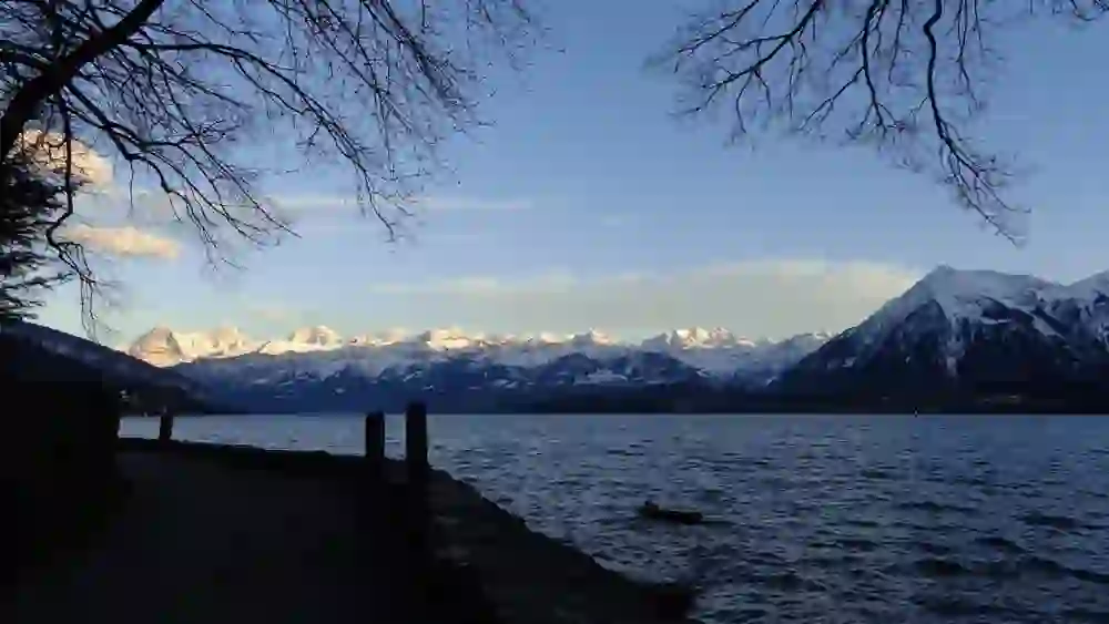 Die ruhige Szenerie einer geführten Nachtwanderung zeigt die majestätischen Schweizer Alpen, die sich im sanften Abendlicht über dem stillen See erheben.