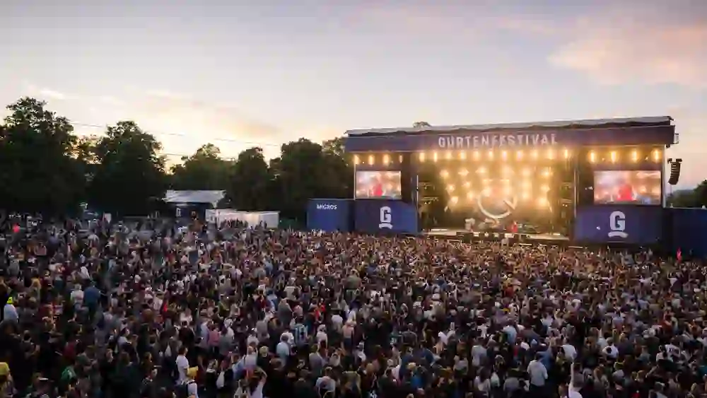 Eine pulsierende Menschenmenge geniesst ausgelassen das Gurtenfestival, im Bann der mitreissenden Live-Musik auf der grossen Bühne, während die letzten Sonnenstrahlen des Tages den Himmel in ein malerisches Abendrot tauchen.