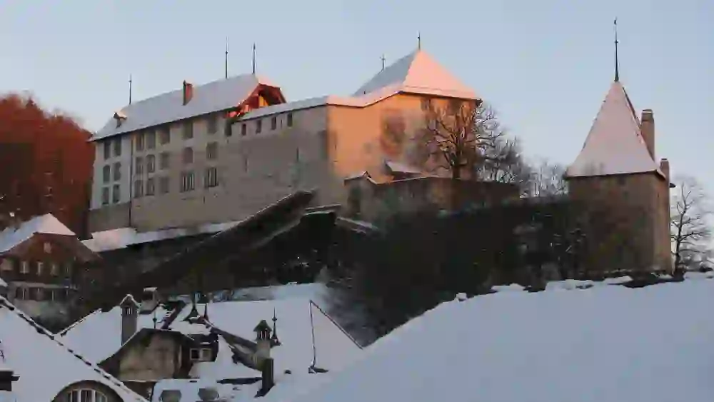 Das Bild zeigt das Schloss Laupen im Winter, bedeckt von Schnee und im warmen Licht der untergehenden Sonne. Die historische Architektur und die schneebedeckten Dächer schaffen eine idyllische und nostalgische Atmosphäre, die Ruhe und zeitlose Eleganz vermittelt.