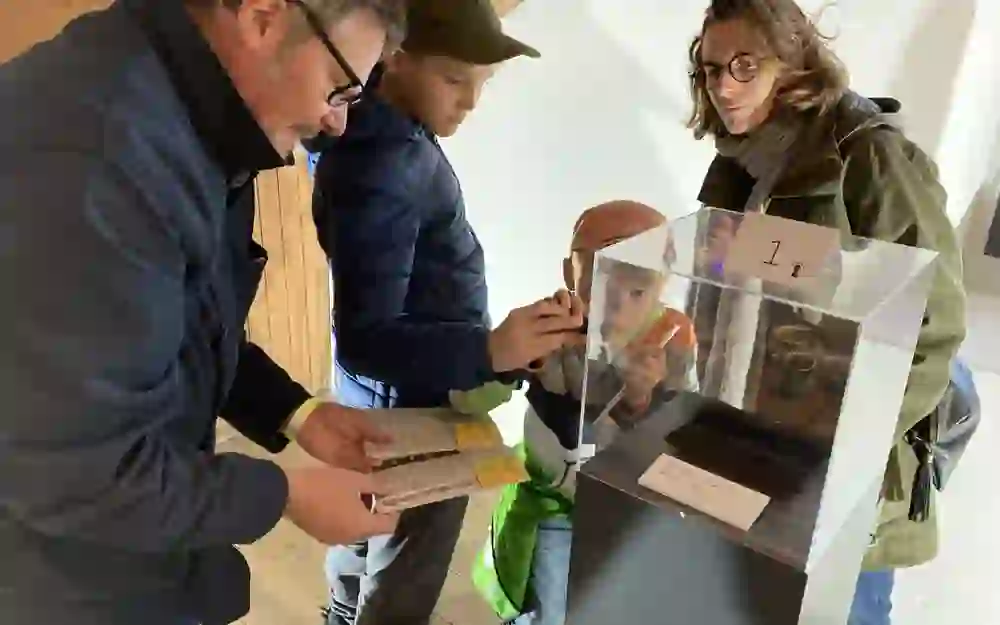 A family explores exhibits together during a detective tour in a museum. The atmosphere is characterised by curiosity and shared learning as they look at details with interest.