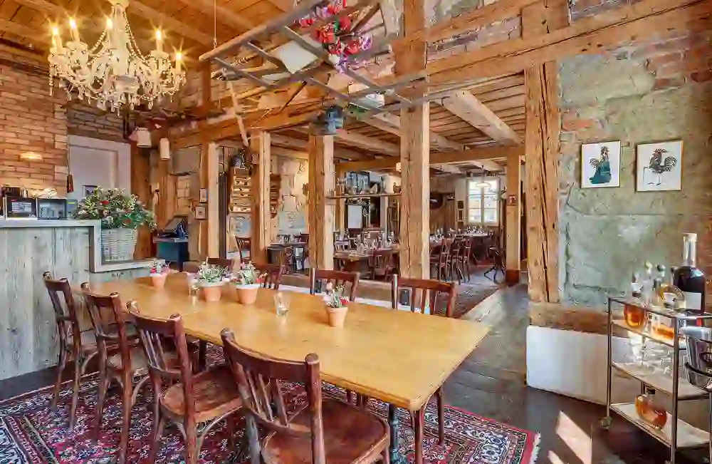 The photo shows an inviting restaurant with rustic décor, wooden furniture and a large chandelier. Flowers on the tables and an oriental rug give the room a warm atmosphere.