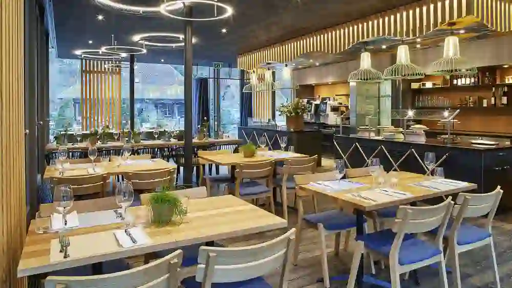 Das Foto zeigt ein modernes Restaurant mit stilvoller Beleuchtung, eleganten Tischen und einer offenen Fensterfront. Es vermittelt eine zeitgenössische und einladende Atmosphäre.
