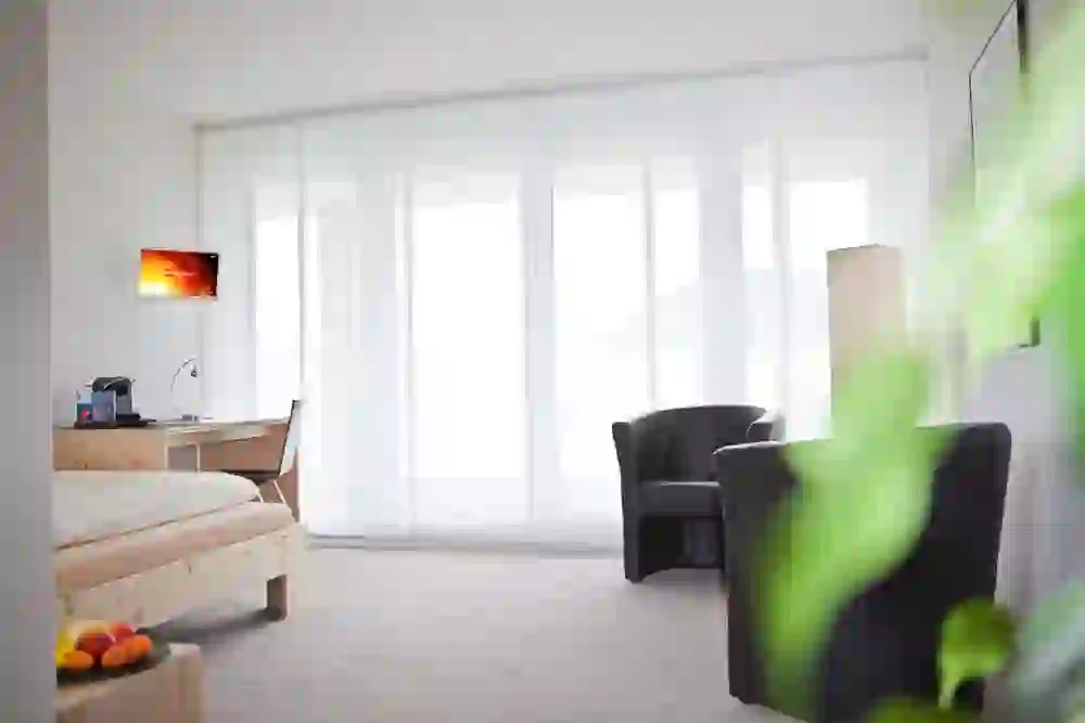 La photo montre une chambre claire et aérée au QCM Campus Belp, avec un mobilier moderne et sobre, de grandes fenêtres et des couleurs douces, qui dégage une atmosphère de calme et de confort moderne.