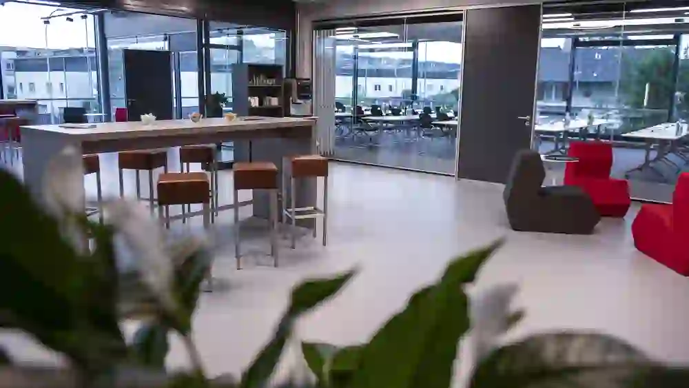 Das Bild zeigt einen modernen, hellen Pausenbereich mit Barhockern und einer Theke, umgeben von entspannenden Sitzgelegenheiten in lebendigem Rot, was eine kreative und dynamische Pause während eines Seminars vermuten lässt.