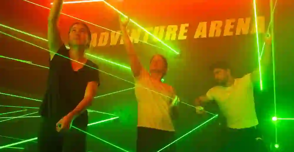 Leuchtende Paintball-Ausrüstungen hängen in Reihen an einer Wand, badend in einer kaleidoskopischen Vielfalt von Neonlichtern, die eine futuristische und aufregende Atmosphäre für ein Teamerlebnis voller Spannung und Spass versprechen.