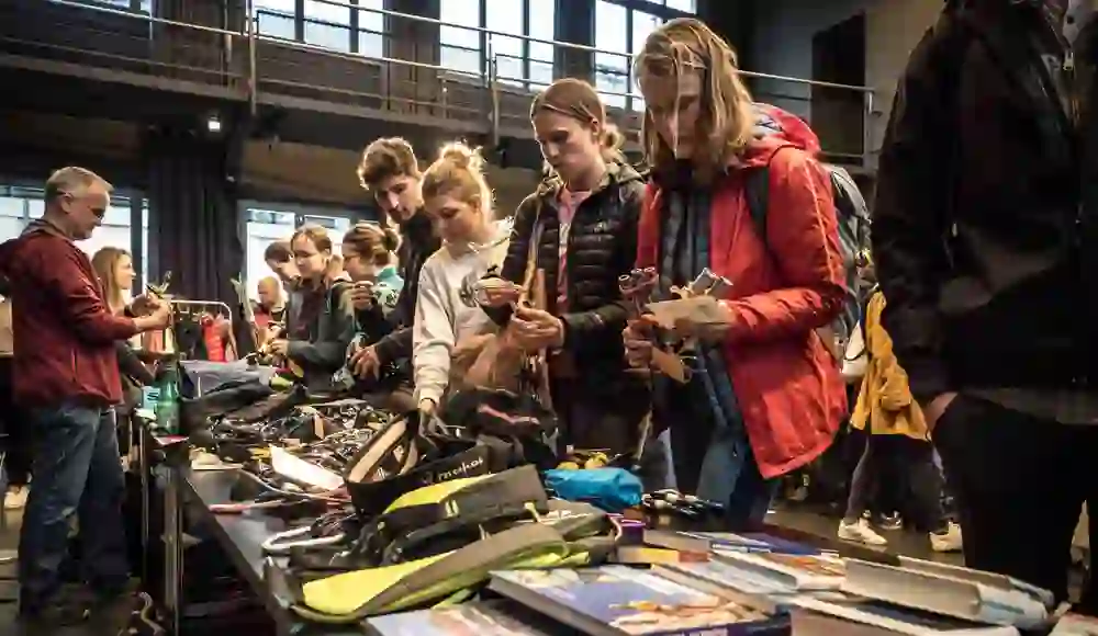 La photo montre l'Alpin Flohmi à l'Alps Bern : des personnes concentrées et curieuses fouillent parmi une multitude d'articles de sport de montagne. Il y a dans l'air une anticipation des aventures à venir - un lieu plein d'échanges, de passion et de découvertes durables.