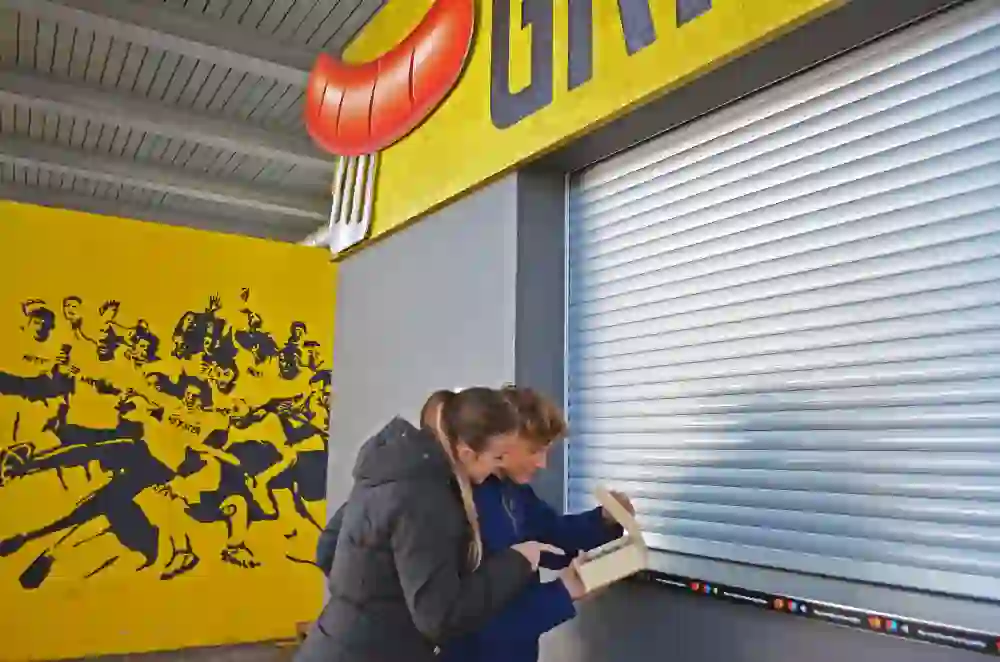 Zwei Personen, vertieft in ein Gespräch, stehen vor einer lebendigen Wandmalerei im Stadion Wankdorf, eingetaucht in die Geschichte des Ortes.