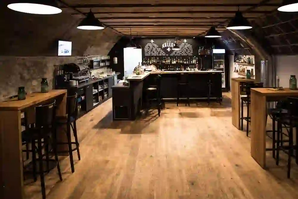 Das Bild zeigt einen gemütlichen Kulturkeller mit warmen Holzböden und Dachbalken, stimmungsvoll beleuchtet und bereit für ein geselliges Beisammensein.