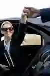 Eine elegant gekleidete Frau steigt lächelnd aus einem schwarzen Auto, während ihr der Chauffeur hilfsbereit die Hand reicht. Die Szene strahlt Professionalität, Stil und zuvorkommende Gastfreundschaft aus.