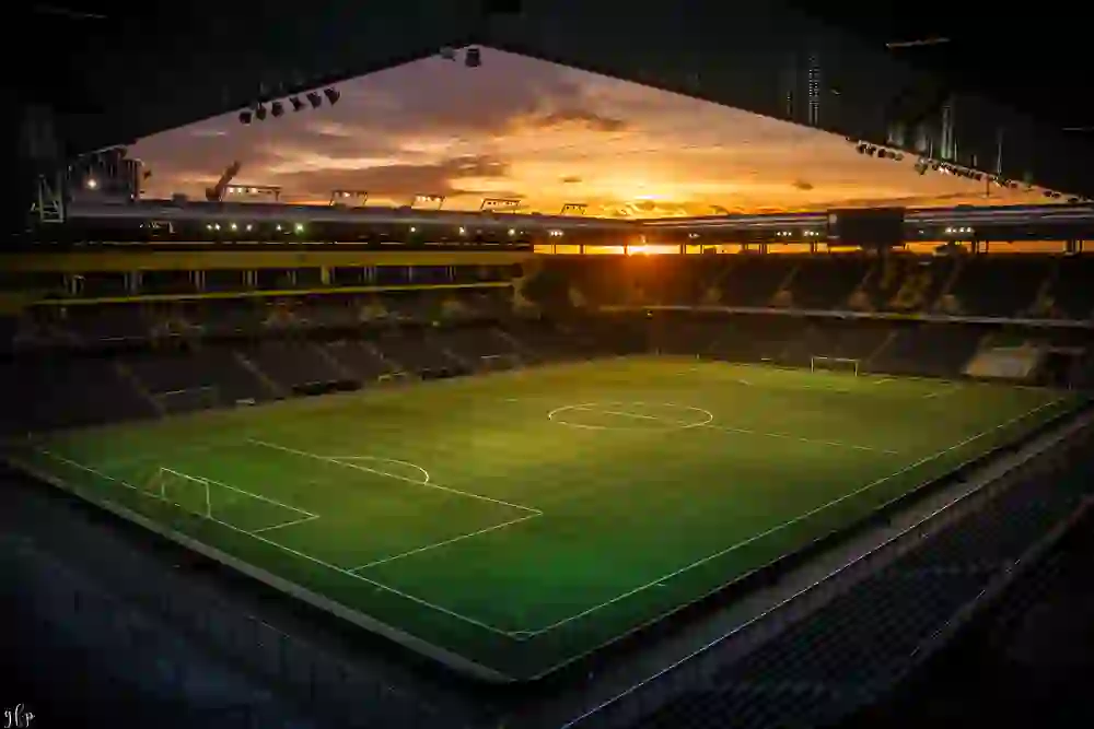 Das Stadion Wankdorf wird vom goldenen Schein eines untergehenden Sonnenhimmels überflutet, der ein Gefühl von Vorfreude und stiller Erwartung auf die nächste Begegnung auf dem grünen Rasen erzeugt.