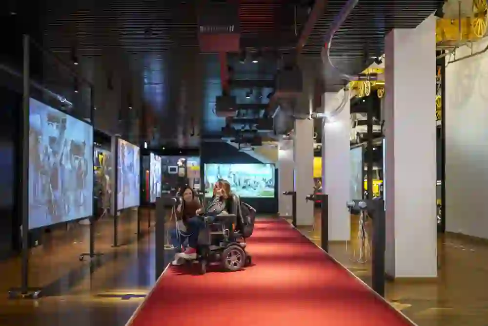 Auf dem Bild sind zwei junge Frauen zu sehen eine ist im Rollstuhl und die beiden hören sich im Museum für Kommunikation etwas an.