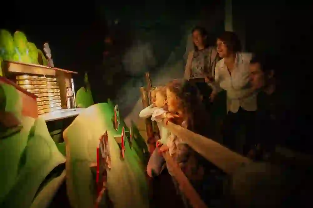 Das Bild zeigt eine Familie, die eine Ausstellung betrachtet, wobei besonders die Kinder mit staunenden Gesichtern gefesselt sind. Die warme Beleuchtung sorgt für eine magische und abenteuerliche Atmosphäre.