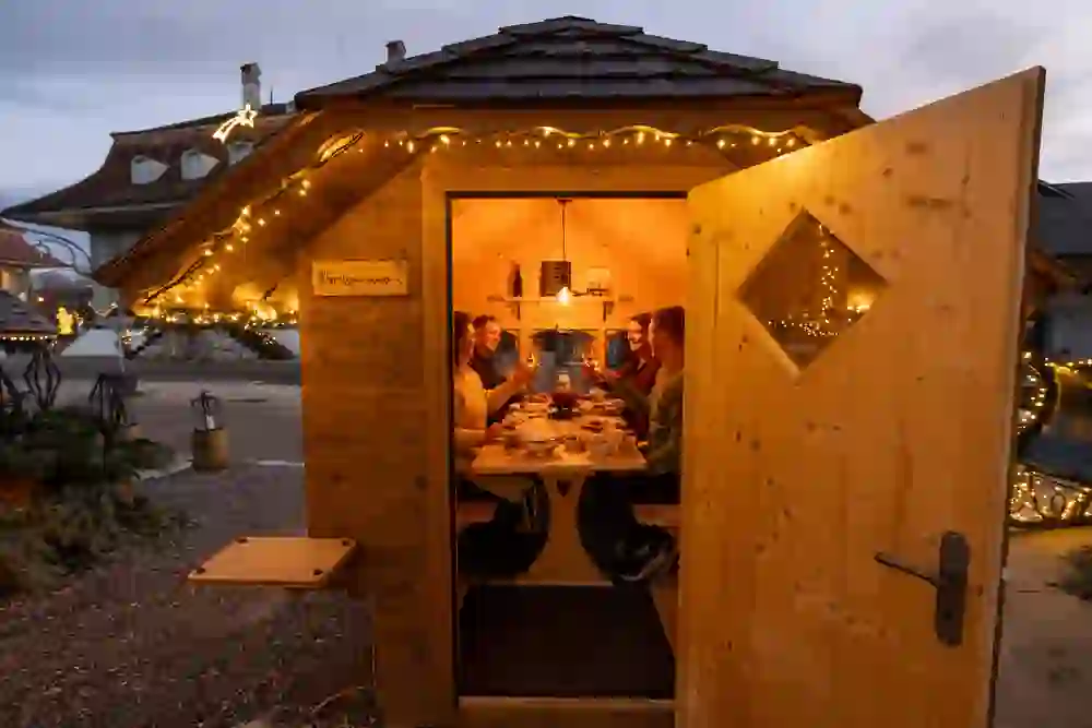 Das Bild zeigt eine gesellige Runde in einem heimeligen Fondue-Spycher des Romantikhotels Bären Dürrenroth, beleuchtet von warmem Licht, das eine gemütliche und freundschaftliche Atmosphäre während der Dämmerstunden schafft.