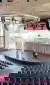 Das Bild zeigt eine beeindruckende Veranstaltungsarena mit halbkreisförmig angeordneten Sitzreihen, die auf eine große Bühne ausgerichtet sind. Das helle Tageslicht strömt durch die Panoramafenster, wodurch der Raum weit und offen wirkt. Die Atmosphäre ist lebendig und bereit für ein bedeutendes Event oder eine Konferenz, wobei die moderne Technik und das große Bühnenbild einen professionellen und feierlichen Rahmen schaffen.
