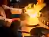 Sur l'image, on voit un cuisinier travailler avec un wok tandis qu'une flamme impressionnante jaillit de la poêle. La chaleur et le feu transmettent la passion et le savoir-faire du cuisinier. L'énergie dans la cuisine est littéralement palpable et donne vie au dynamisme de la cuisine asiatique.