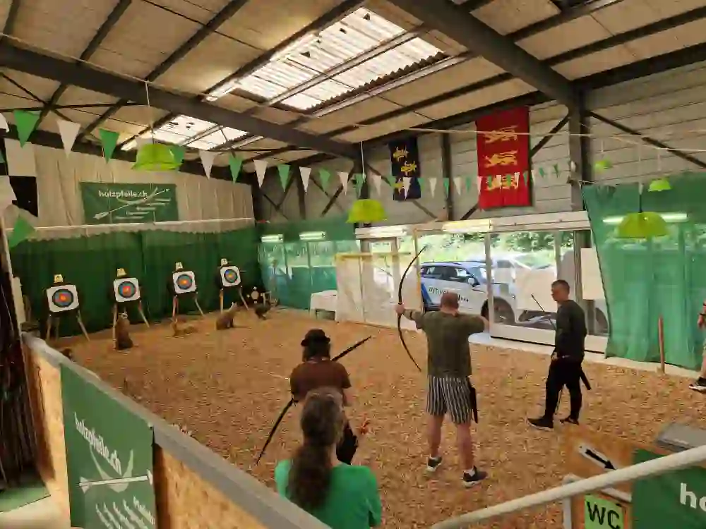 Das Bild zeigt Personen in einer Bogenhalle welche gerade Bogenschiessen als Teamevent oder Gruppenaktivität