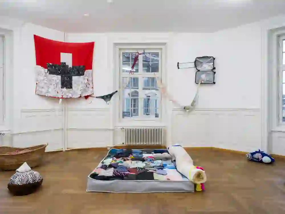 Das Bild zeigt ein interessantes Raumkonzept im Kunsthaus Langenthal. Es sieht so aus, als wäre die Installation mit Alltagsgegenständen und Textilien geschaffen, was dem Raum eine sehr persönliche und fast wohnliche Note gibt.