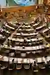 Das Bild zeigt den Schweizer Nationalratssaal in seiner vollen Pracht. Die geschwungenen Sitzreihen, gefüllt mit konzentrierten Abgeordneten, spiegeln die Dynamik und Ernsthaftigkeit politischer Diskussionen wider. Die Atmosphäre ist förmlich, doch geprägt von Engagement.