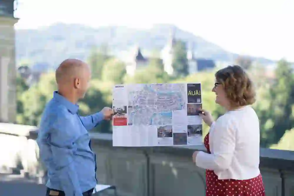 Deux personnes regardent une grande carte de Berne. L'atmosphère décontractée et l'environnement ensoleillé suggèrent une planification détendue des vacances avec un décor historique en arrière-plan.