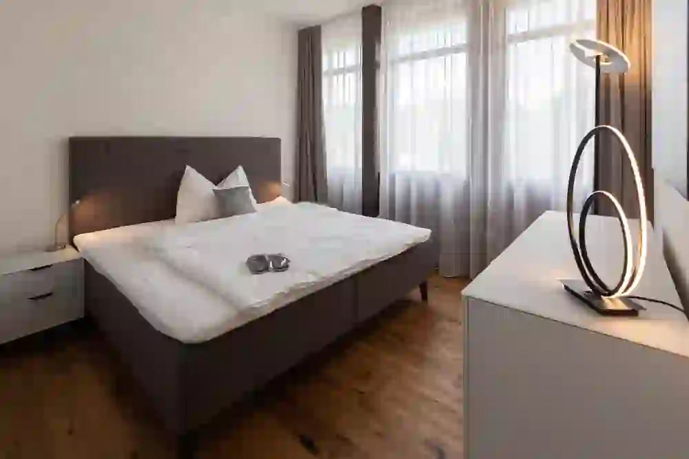 Das Bild zeigt ein geschmackvoll eingerichtetes Schlafzimmer im Glandon Aparmtments mit einem grossen, einladenden Bett und stilvoller Beleuchtung. Die Atmosphäre ist friedlich und beruhigend, perfekt für eine erholsame Nachtruhe.