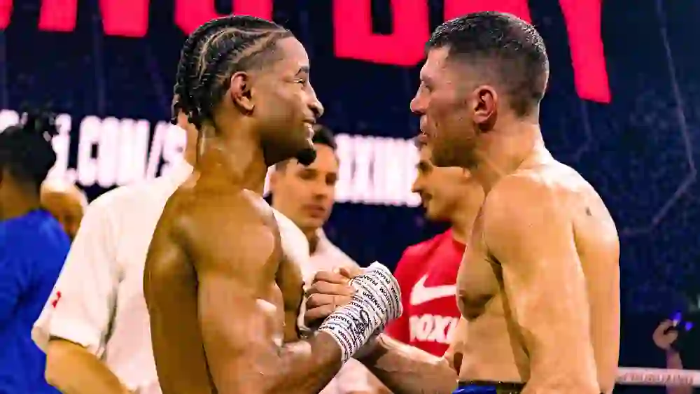 L'immagine mostra due pugili esausti ma rispettosi dopo un intenso incontro. Si guardano dritto negli occhi e si stringono la mano, segno di rispetto reciproco. L'atmosfera è piena di ambizione, orgoglio e correttezza sportiva.