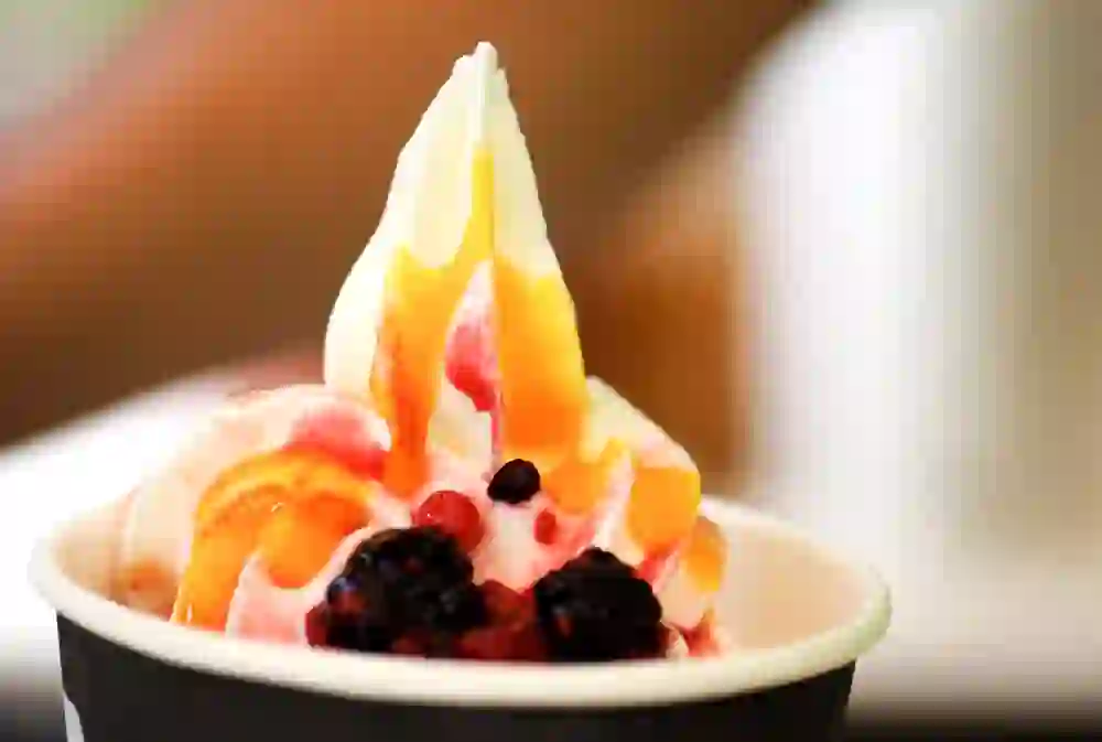 Das Bild präsentiert ein appetitliches, farbenfrohes Softeis mit Beerentopping und fruchtigen Saucen, das in einem Becher serviert wird und zum Genießen einlädt.