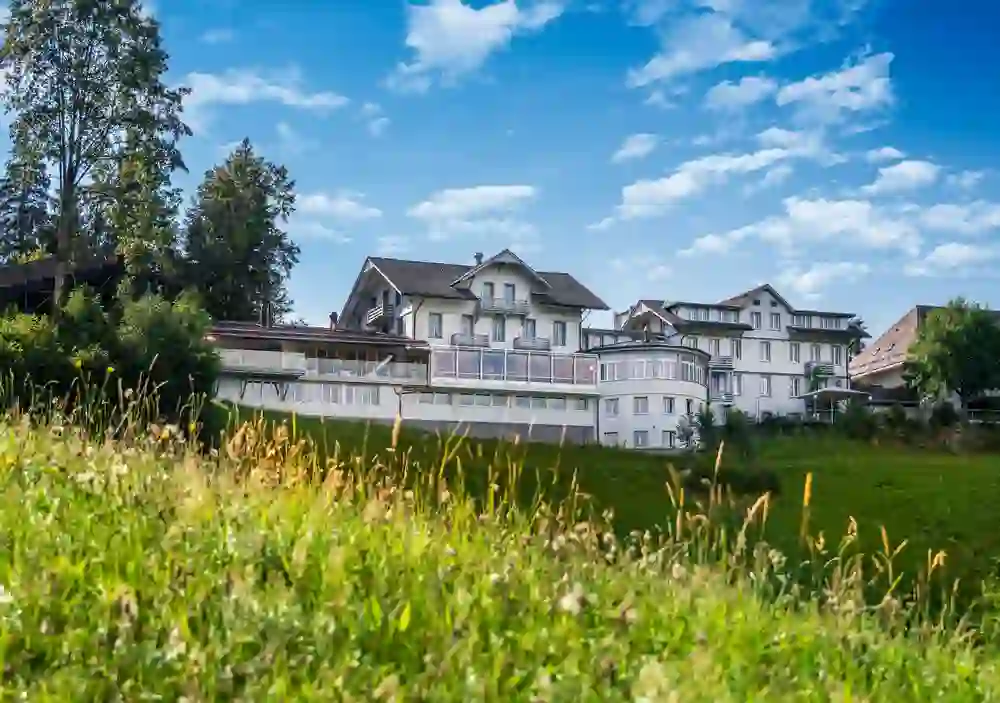 The picture shows the Hotel Moosegg in idyllic surroundings, embedded in green nature, shining under a clear blue sky, which conveys a peaceful and refreshing atmosphere.