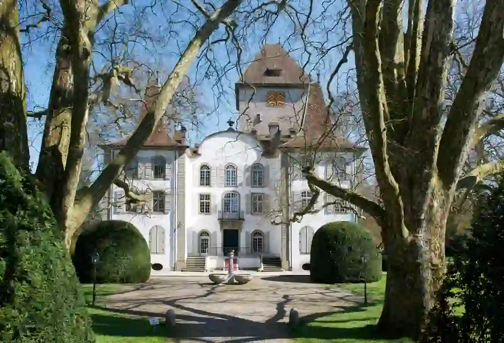 Das Bild zeigt das Schloss Jegenstorf, ein prächtiges weisses Gebäude mit einem klassischen, steilen Dach, eingebettet in eine ruhige, grüne Parklandschaft, die Ruhe und historische Eleganz ausstrahlt.