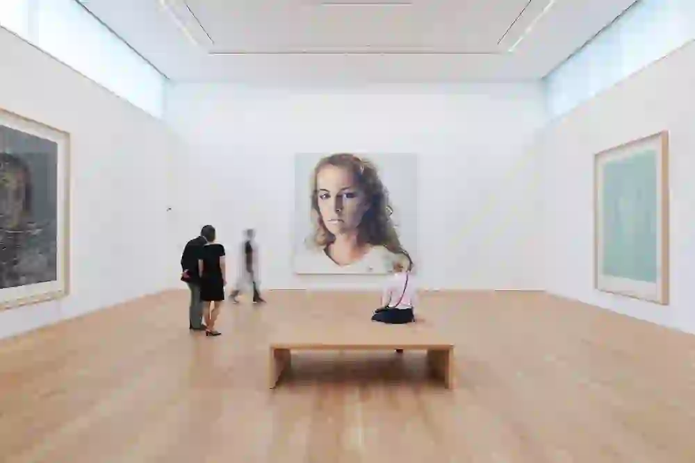 The photo shows a scene in the Franz Gertsch Museum with visitors looking at a large-format portrait. The person on the bench, absorbed in contemplation, emphasises the calm and introspective atmosphere. The natural light lends the room a peaceful atmosphere.