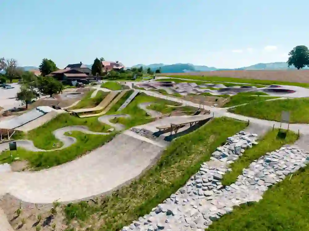 A sunny day in the Swiss Bike Park Oberried, where an artfully designed pump track invites you to enjoy fast bike laps. The landscape exudes tranquillity, while the trails promise adventure.