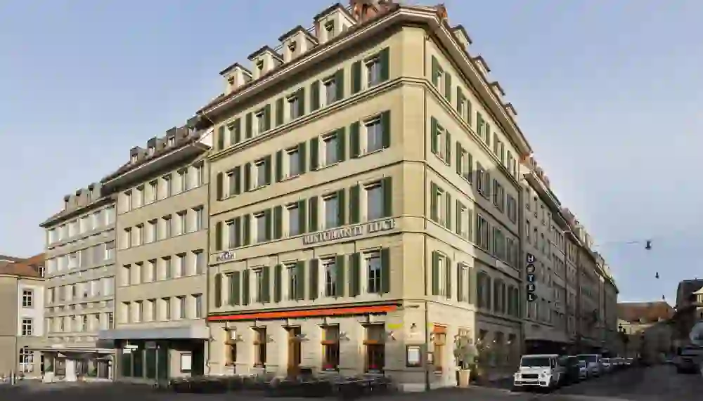 The picture shows the outside of the Hotel Stay Kooook Bern City in Bern's old town. The sun is shining and gives a warm light to the stone façade.