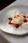 An artfully arranged dessert on a white plate: strawberries, fine meringue and delicate flowers adorn the creamy centre. The scene appears calm, elegant and lovingly composed - a moment of pure pleasure.