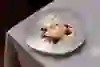 An artfully arranged dessert on a white plate: strawberries, fine meringue and delicate flowers adorn the creamy centre. The scene appears calm, elegant and lovingly composed - a moment of pure pleasure.