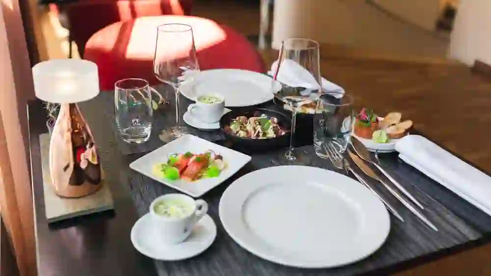 Das Bild zeigt ein fein gedecktes Tischarrangement im Restaurant mille sense in Bern mit einer warmen, einladenden Atmosphäre. Verschiedene Gerichte, darunter ein Salat, eine Suppe und ein Fischgericht, sind ansprechend präsentiert und erwarten den Gast.