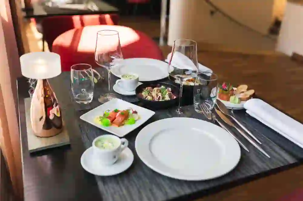 The picture shows a finely laid table arrangement in the restaurant mille sense in Bern with a warm, inviting atmosphere. Various dishes, including a salad, a soup and a fish dish, are attractively presented and await the guest.