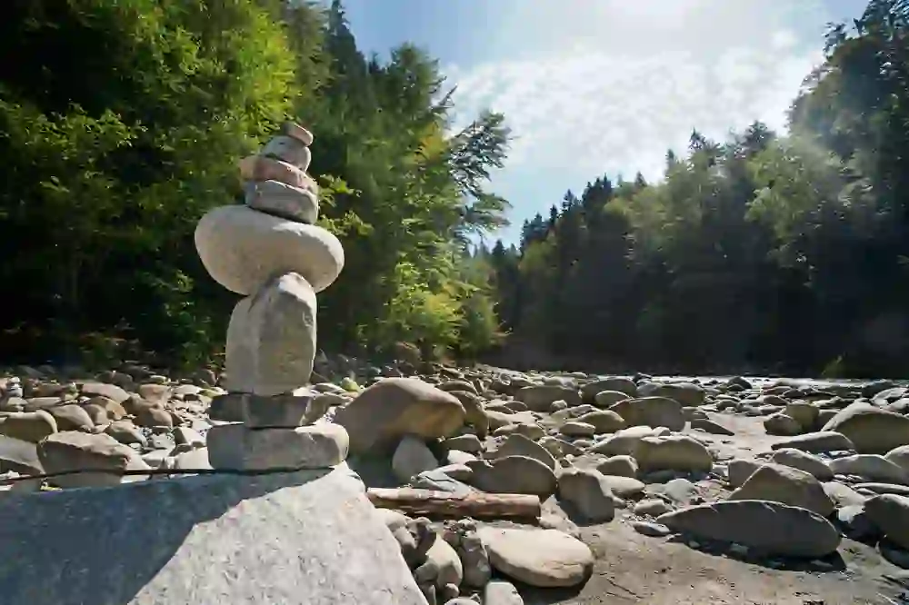 Ein Steinmann steht am Ufer der Emme, ein Bild von Frieden und Ausgeglichenheit inmitten des flüsternden Flusses und des dichten Grüns, das die Sinne beruhigt.