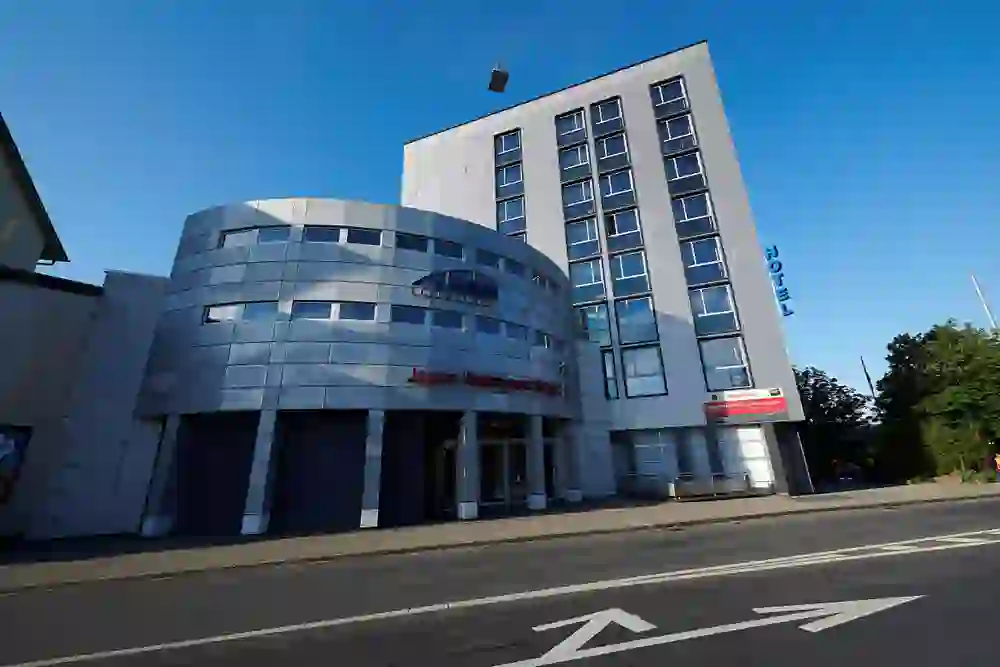 The photo shows the modern building of the Hotel Ambassador in Bern, characterised by clear lines and a smooth façade that radiate an urban and contemporary atmosphere under a bright blue sky.