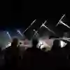Un moment de festival la nuit : les gens regardent le ciel avec enthousiasme tandis que des fusées de feu d'artifice explosent en trajectoires lumineuses. La musique, les acclamations et l'ambiance lumineuse magique plongent la foule dans l'euphorie.