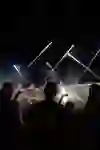 Un moment de festival la nuit : les gens regardent le ciel avec enthousiasme tandis que des fusées de feu d'artifice explosent en trajectoires lumineuses. La musique, les acclamations et l'ambiance lumineuse magique plongent la foule dans l'euphorie.