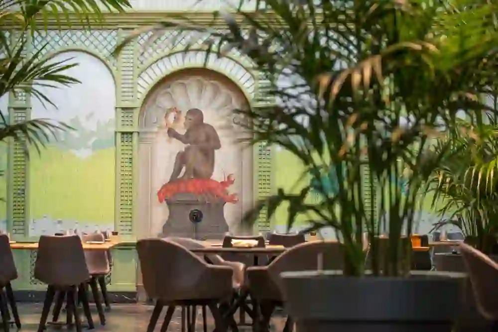 The picture shows the elegant interior of the Zum Äusseren Stand restaurant in Bern, with tropical plants and a mural that creates a playful contrast to the classic elegance of the surroundings.