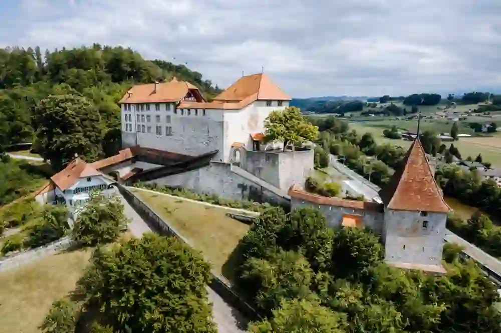 Das Luftbild zeigt das majestätische Schloss Laupen, umgeben von üppigem Grün und einer sanften Hügellandschaft. Die robusten Mauern und spitzen Türme strahlen Stärke aus, während das friedliche Panorama ein Gefühl von zeitloser Ruhe und Beständigkeit vermittelt.